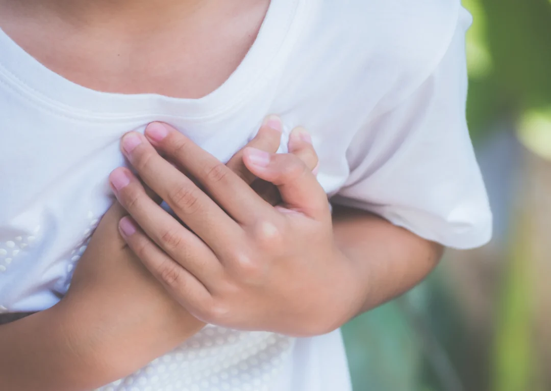 Young boy in white t-shirt clutches heart, indicating heart condition.
