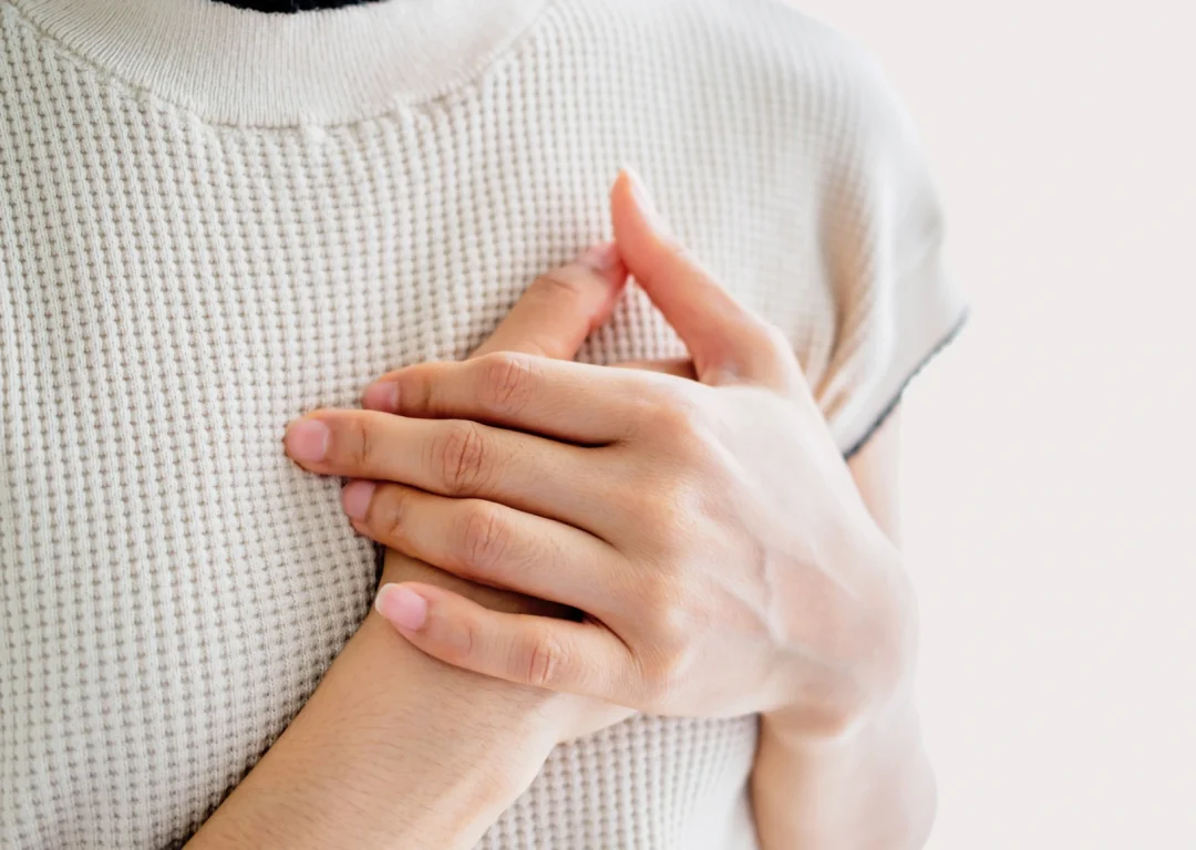 Girl in whit knit top has hands on her heart, indicating heart condition.