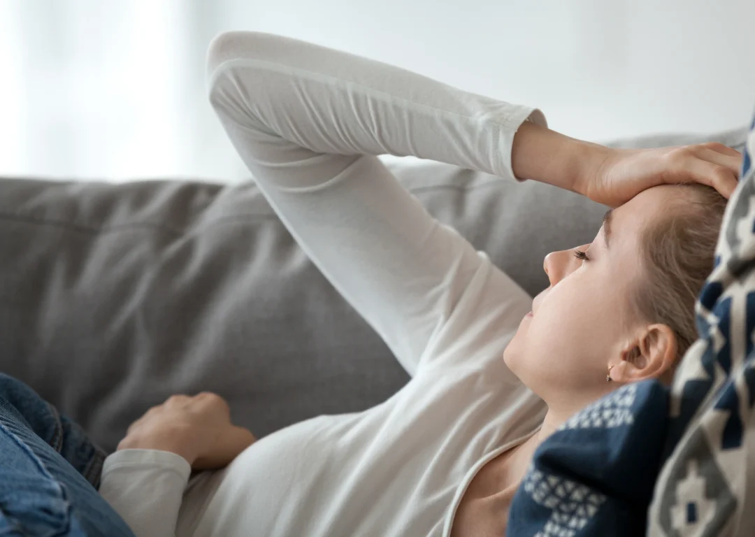 Teenage girl lies on sofa, feeling fatigued due to heart condition.