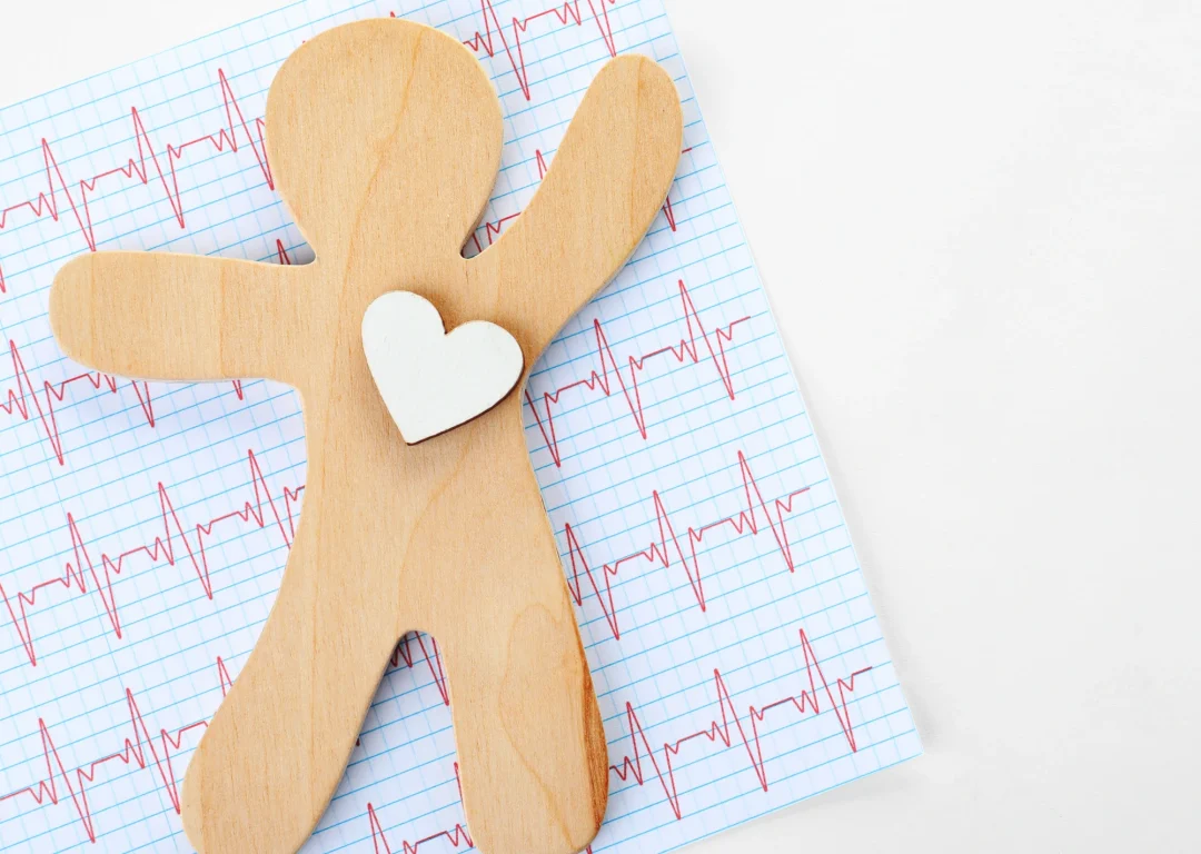 Wooden figure with heart ornament on top of ECG readings.