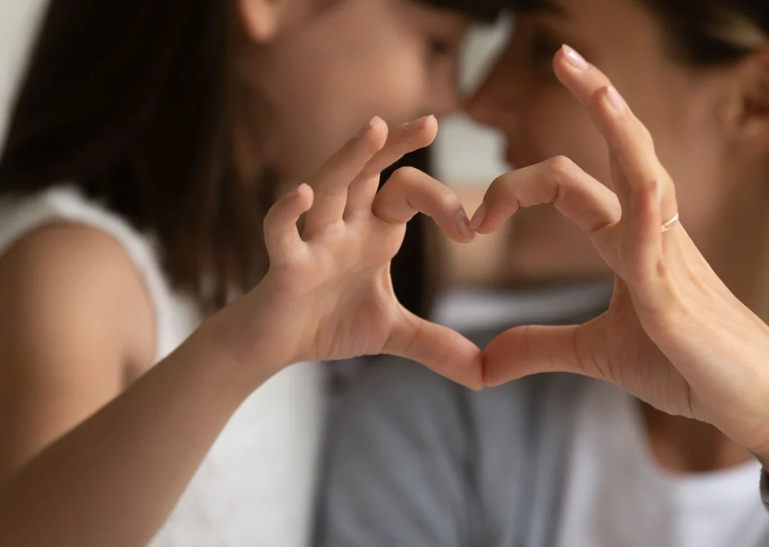 Mother and young daughter making a heart shape with their hands.