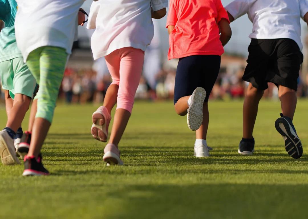 Children in bright coloured sports clothes running in a field.