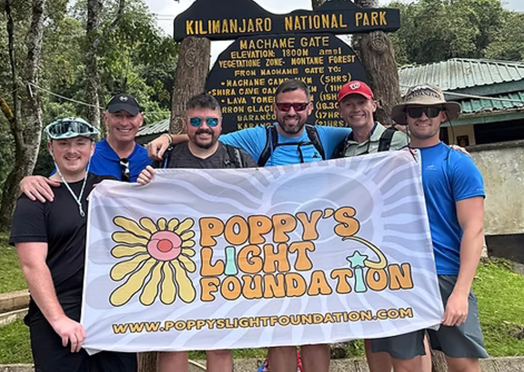 The Poppy's Light Foundation team holding a flag with the logo at the start of the Kilimanjaro trail.