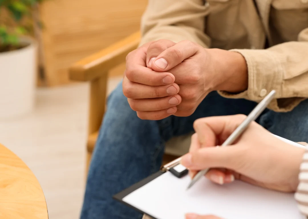 Close up of hands of a young man and a therapist holding a pen and clipboard during therapy session.