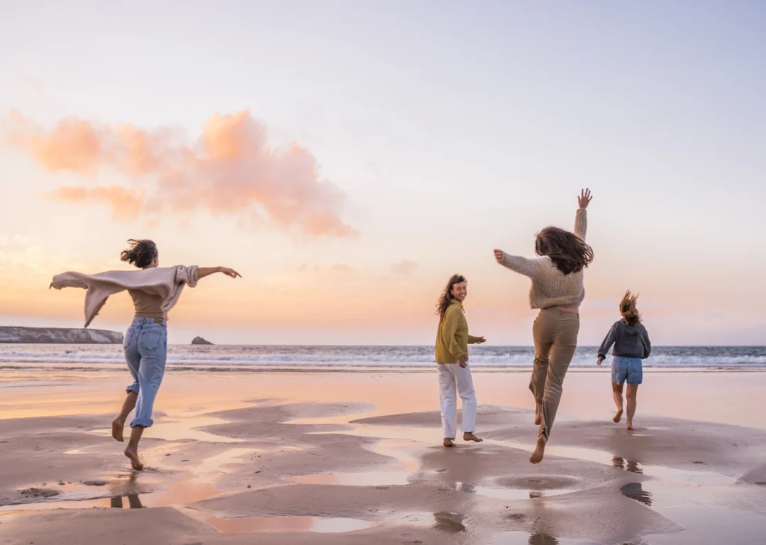 Young women running on beach together with pink sunset in background.