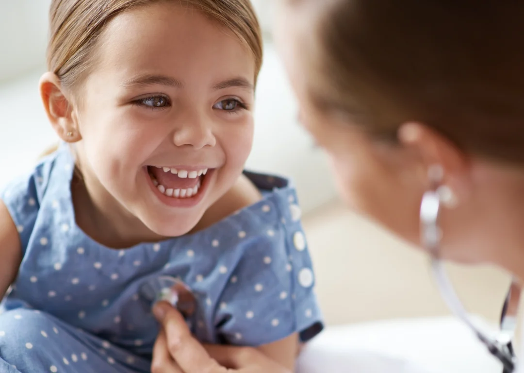Young smiling girl having examination by doctor listening to her heart with stethoscope.