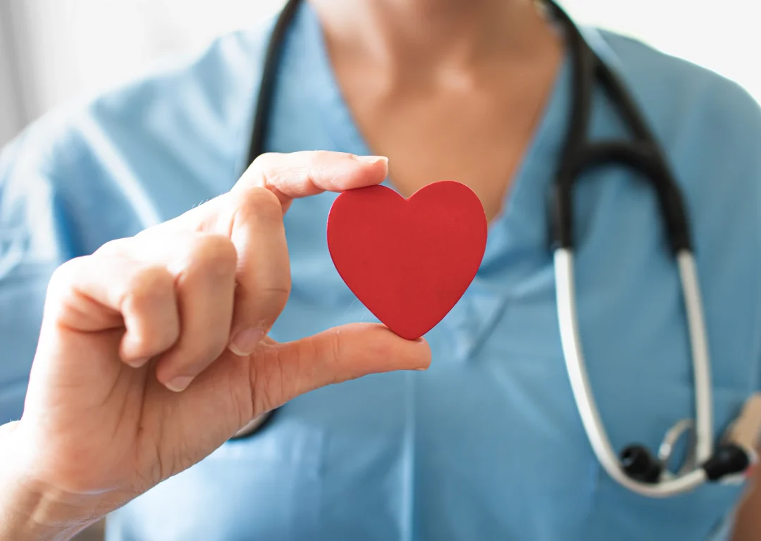 Nurse wearing blue and holding a red paper heart.