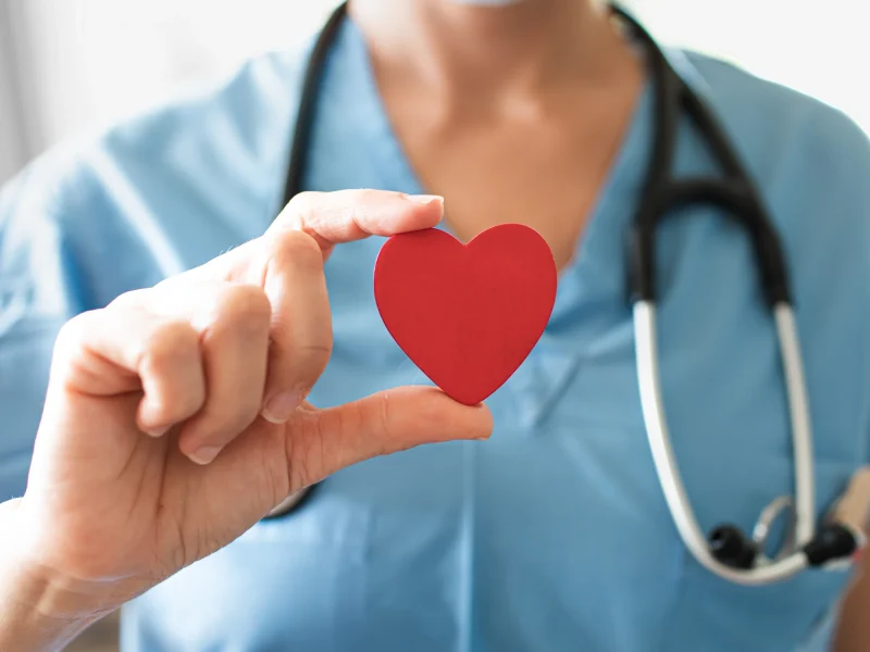 Nurse wearing blue and holding a red paper heart.